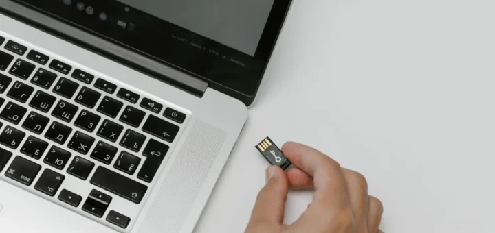 Dłoń trzymająca niewielką pamięć USB obok otwartego laptopa