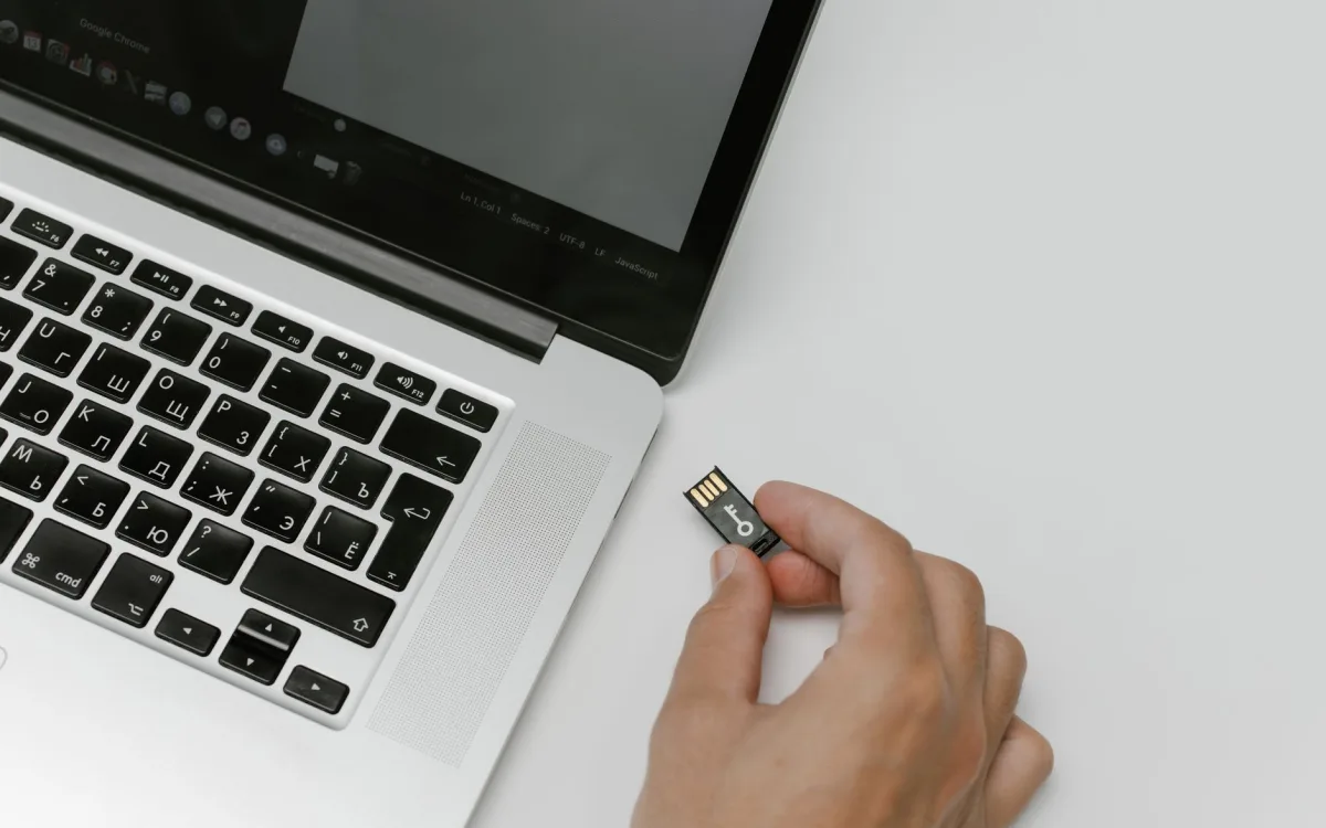 Dłoń trzymająca niewielką pamięć USB obok otwartego laptopa