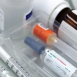 Strzykawki i ampułki w plastikowej tacce obok butelek z lekami