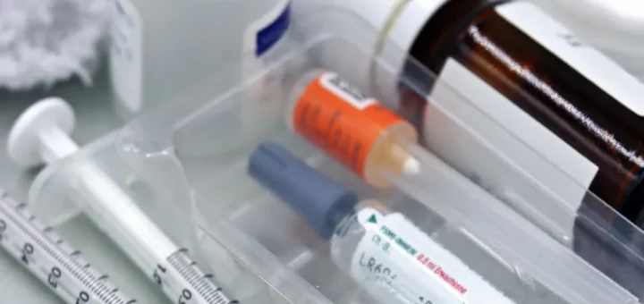 Strzykawki i ampułki w plastikowej tacce obok butelek z lekami