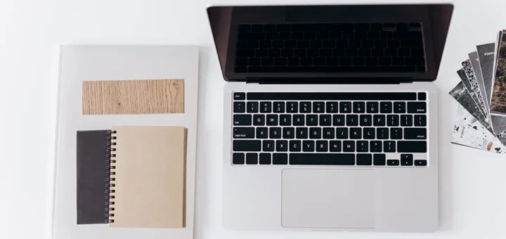 Laptop, notes w spirali i próbnik drewna ułożone na białym blacie, widok z góry