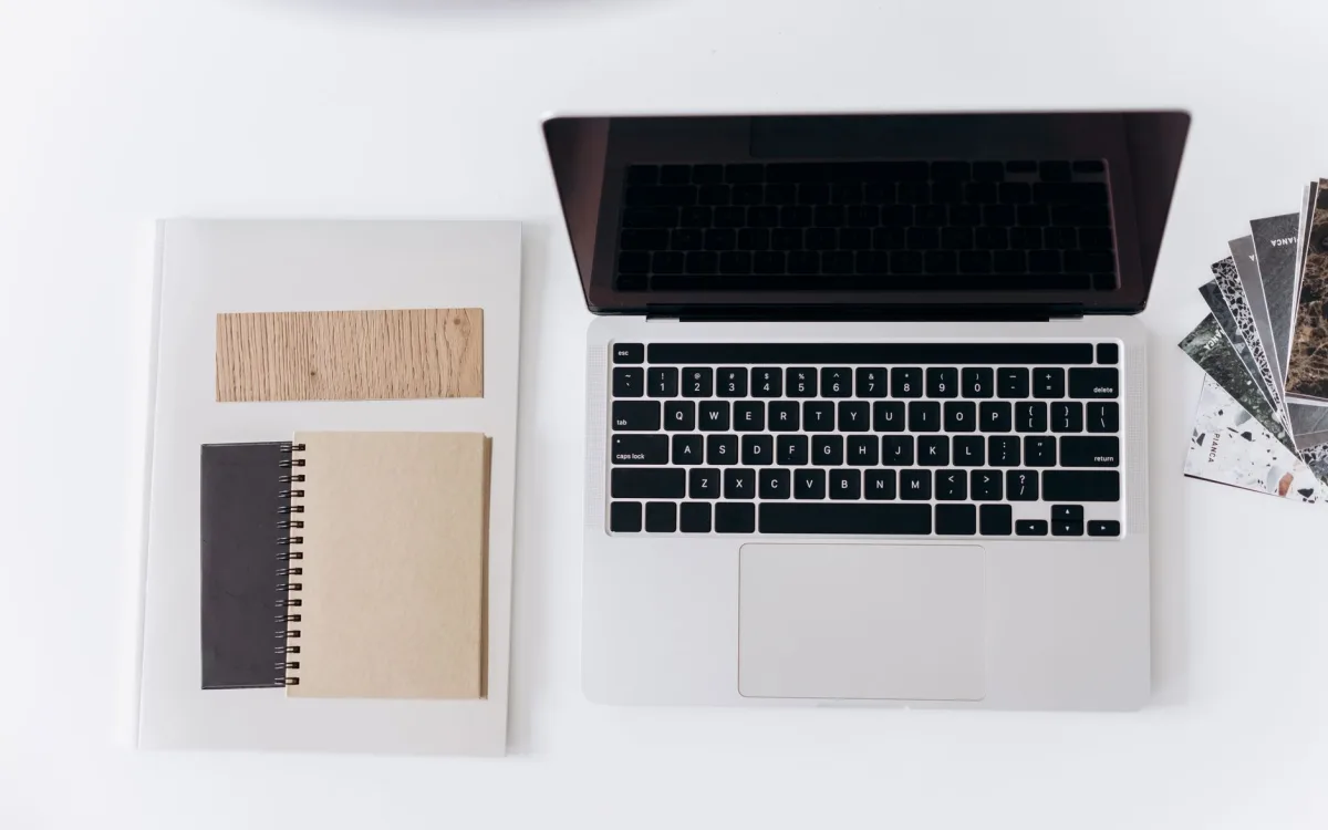 Laptop, notes w spirali i próbnik drewna ułożone na białym blacie, widok z góry