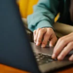 Dłonie na klawiaturze laptopa przy drewnianym biurku, zbliżenie