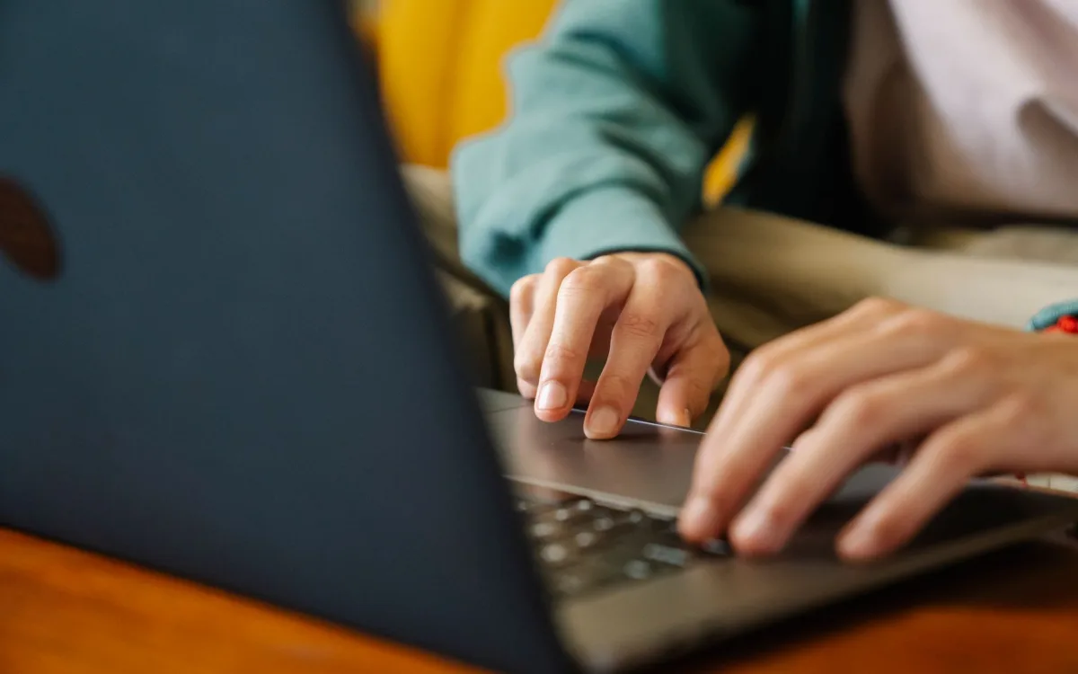 Dłonie na klawiaturze laptopa przy drewnianym biurku, zbliżenie